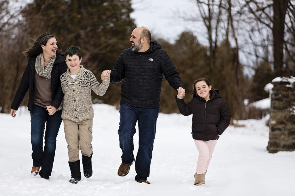 parents hold hands with two children while they skip in the snow