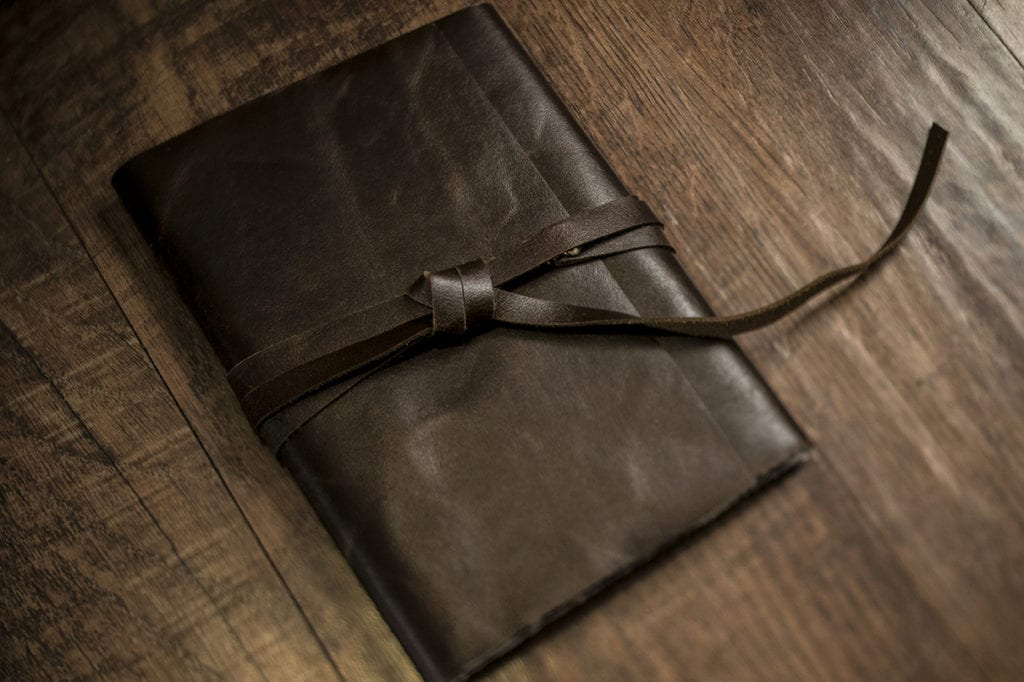 Leather strap knotted around dark leather satchel containing modern Ontario wedding photos