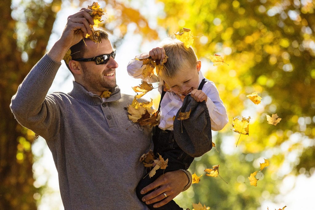 dad throws leaves on son's head while holding him during session with ontario family phtographer