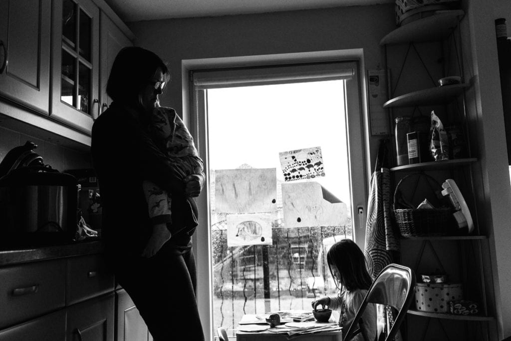 mother holds child in window light while looking down at daughter