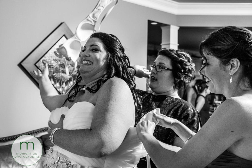 bride tosses bra behind her while bridesmaids help her with her dress