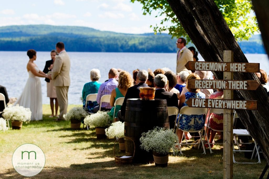 love is everywhere sign at end of aisle while bride and groom get married during waterfront Lake Calabogie wedding