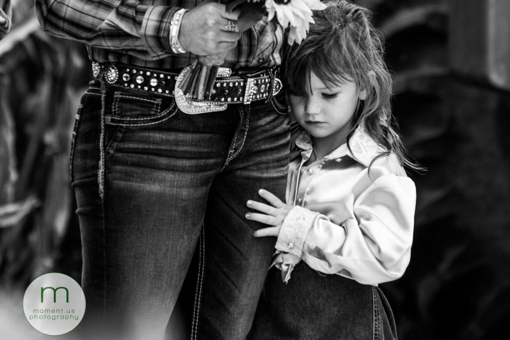 flower girl stands close to bridesmaid and holds her leg during rural Ontario wedding ceremony