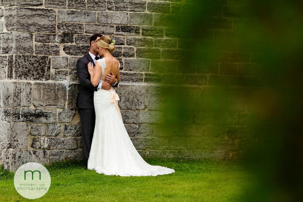 groom leans against stone wall and holds bride close during Ontario & Quebec Wedding Photography portraits