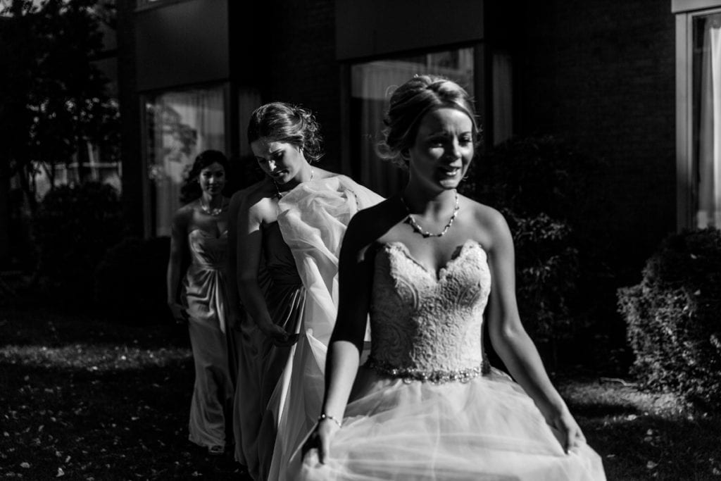 bridesmaids help bride carry dress in dramatic sunlight for Autumnal NAV Centre Cornwall Wedding