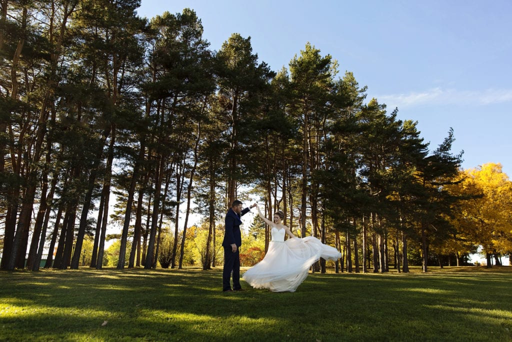 groom twirls bride in blush wedding dress in front of pines
