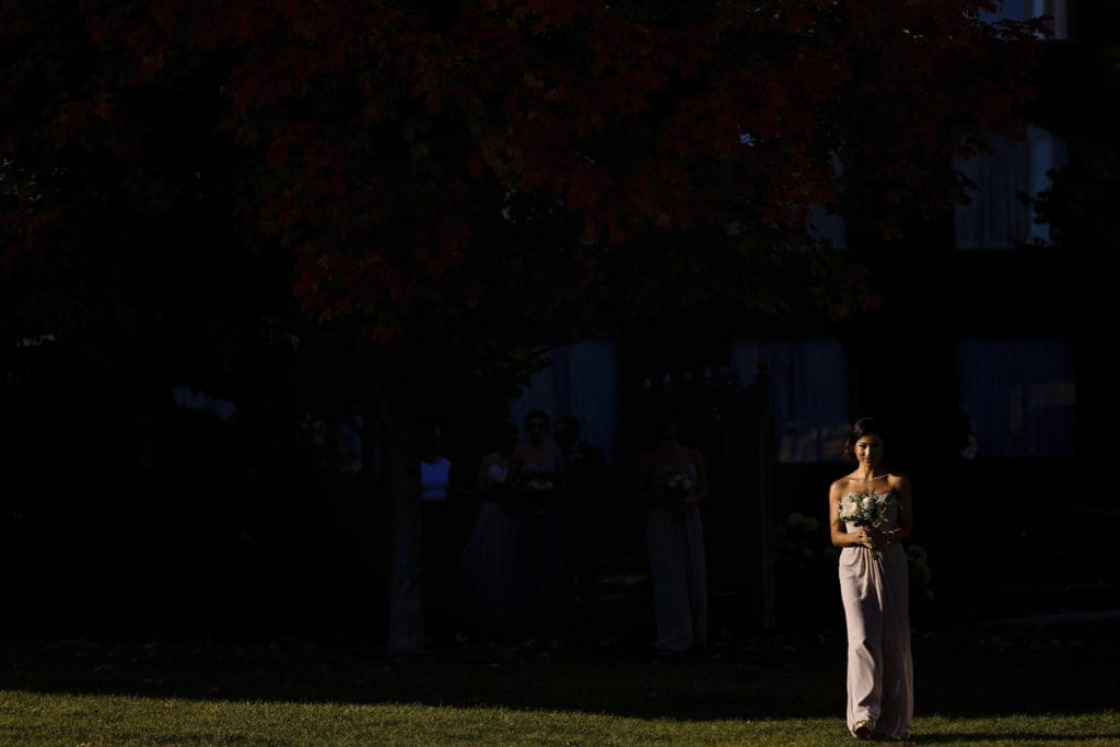 bridesmaid walks down aisle in dramatic sunlight for Autumnal NAV Centre Cornwall Wedding