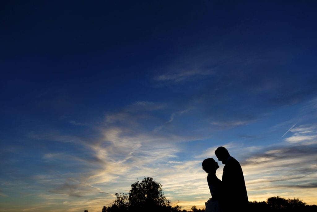 bride and groom in silhouette against blue and yellow sunset