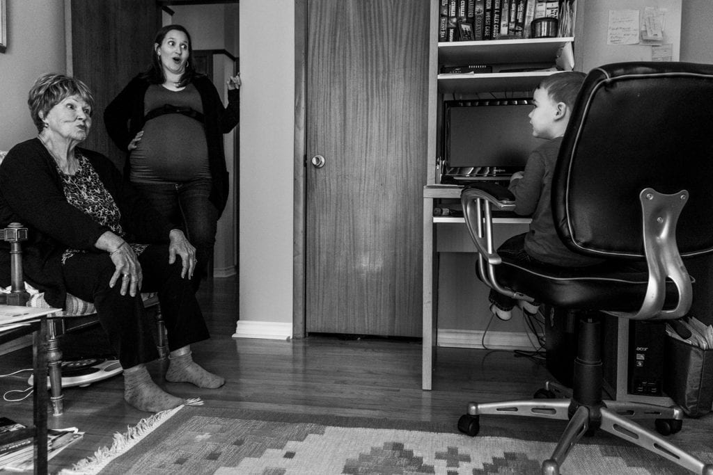 mother and grandma look surprised while talking to boy in office chair during Ontario Family Photojournalism session