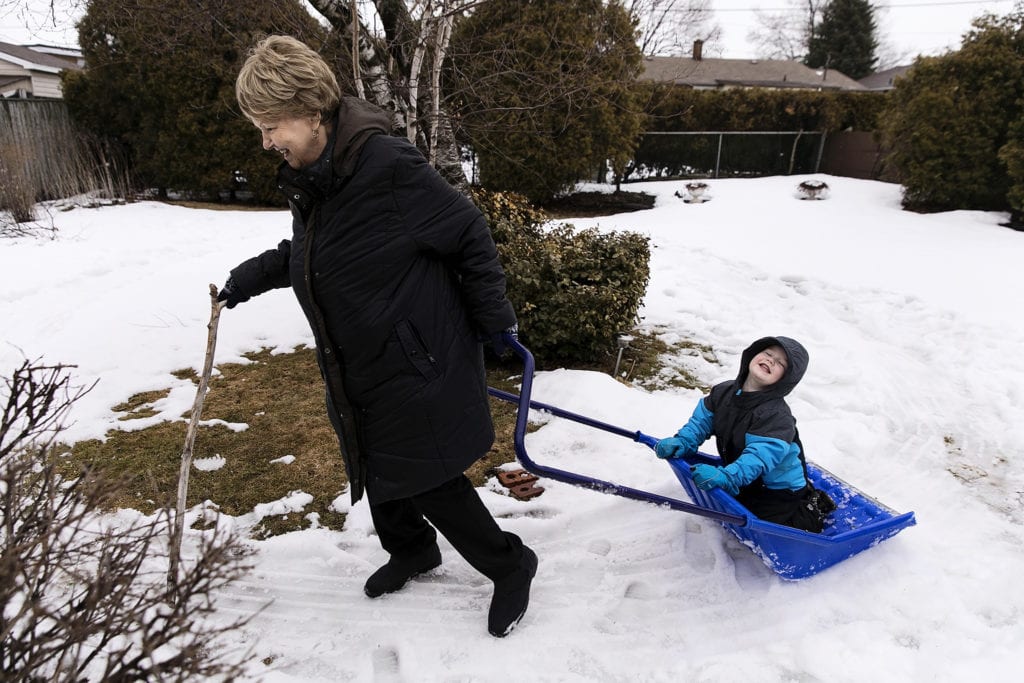 grandma holds walking stick and pulls grandson on shovel during Ontario Family Photojournalism session