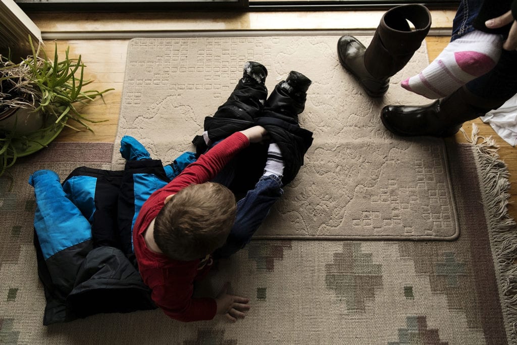boy puts on snow boots while mother does the same beside him