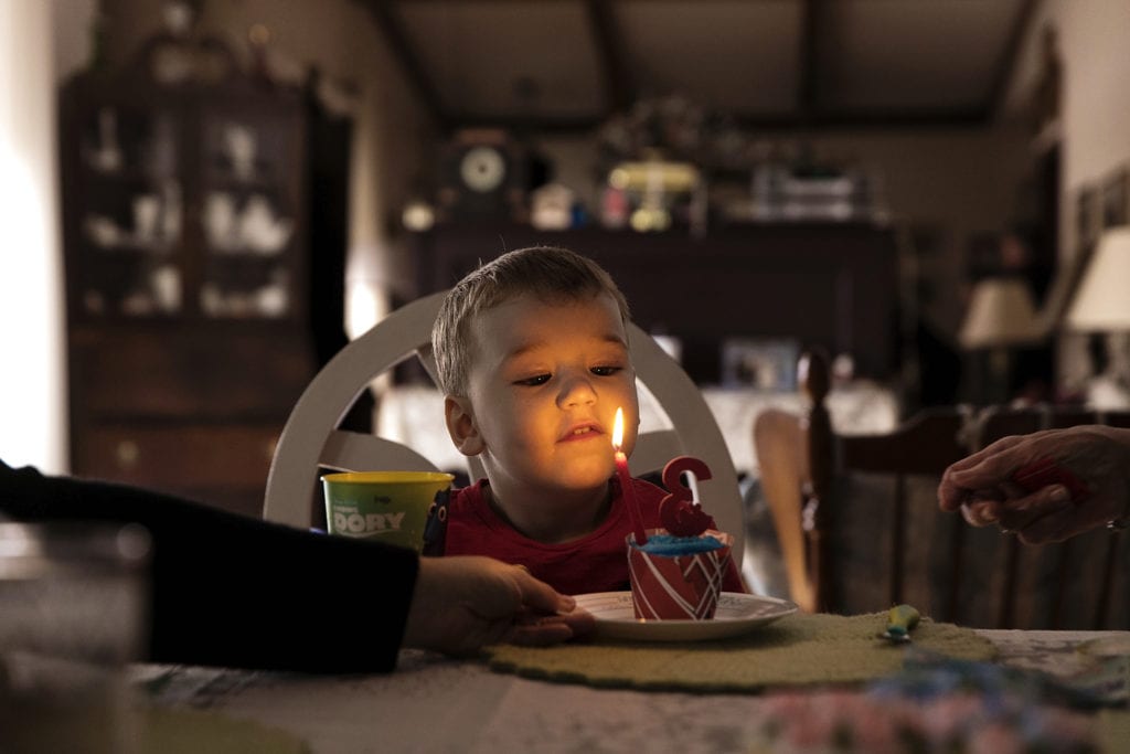 boy's face lit by birthday candles on cupcake during Ontario Family Photojournalism session