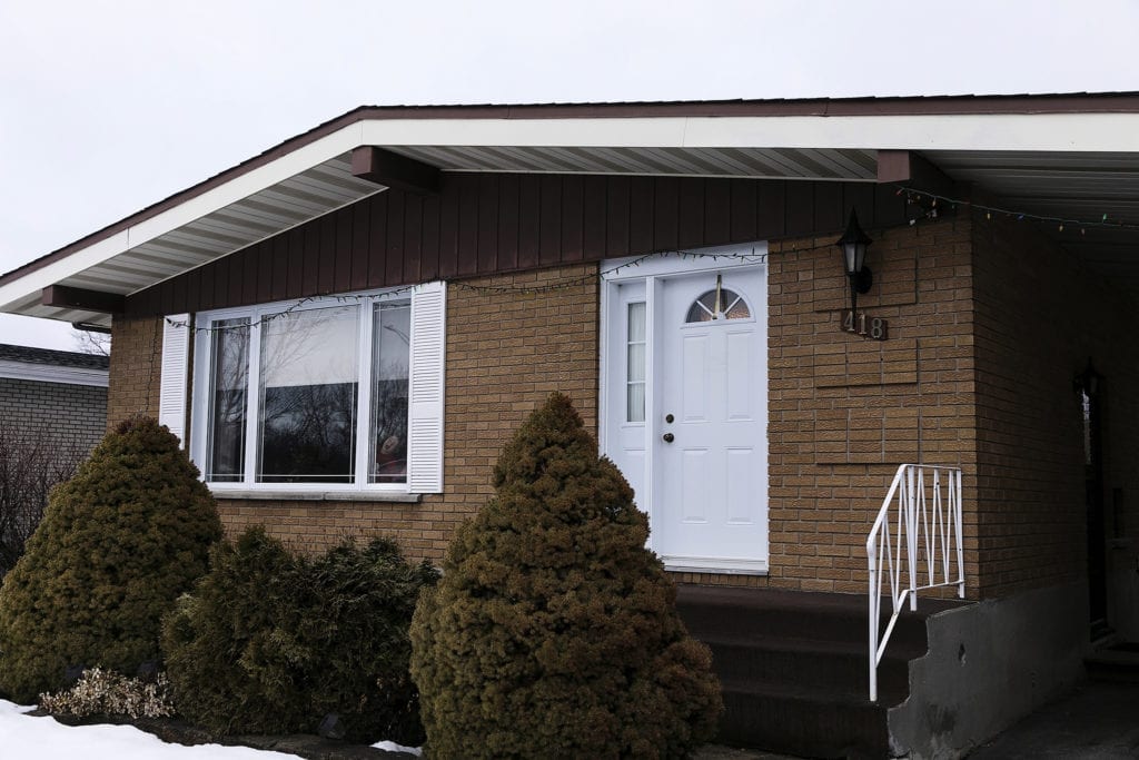 boy stands in window of grandparents' house during Ontario Family Photojournalism session