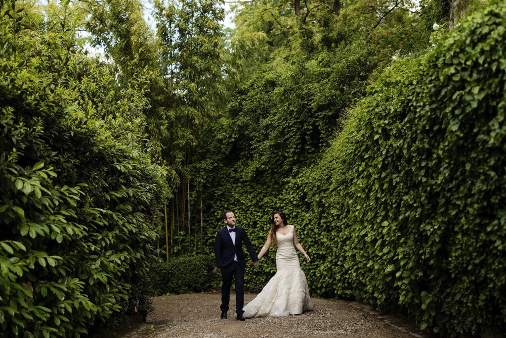 bride and groom walk up driveway surrounded by hedges during session with Ontario & Destination Wedding Photographer