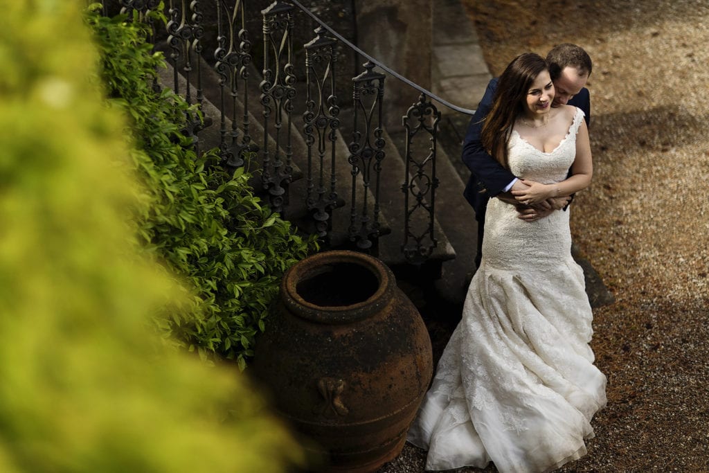 groom cuddles bride from behind in front of italian villa staircase during session with Ontario & Destination Wedding Photographer