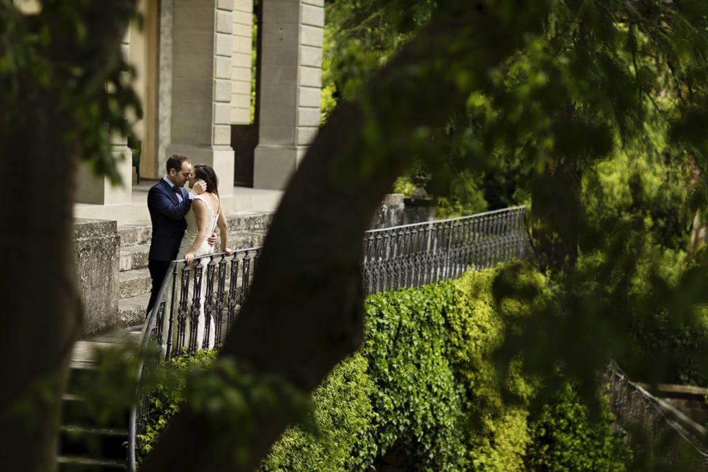 groom strokes bride's cheek while she leans against villa's terrace railing during session with Ontario & Destination Wedding Photographer