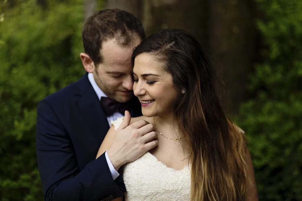 groom strokes bride's collarbone while standing behind her during session with Ontario & Destination Wedding Photographer