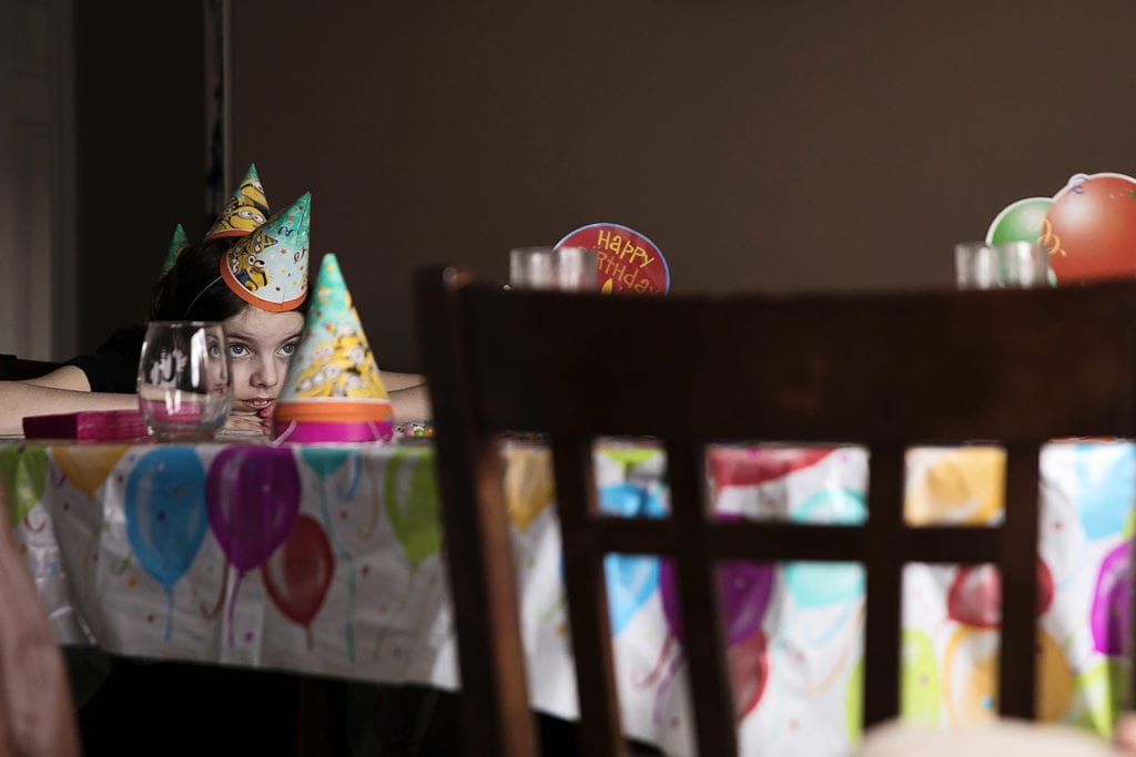 girl rests head on table while wearing three party hats like a stegosaurus