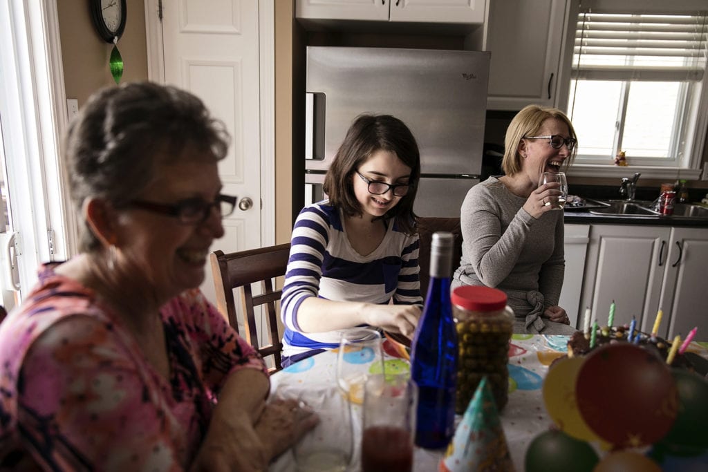 women laughing together around kitchen table during Eastern Ontario family photojournalism session