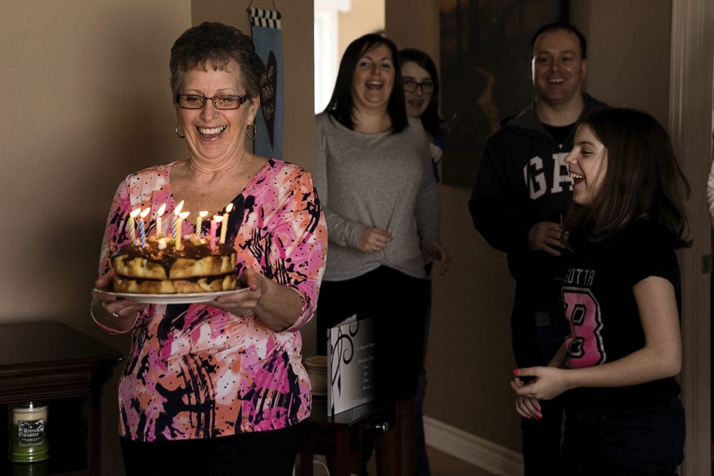 mother carries cake lit with candles while grinning widely during Eastern Ontario family photojournalism session