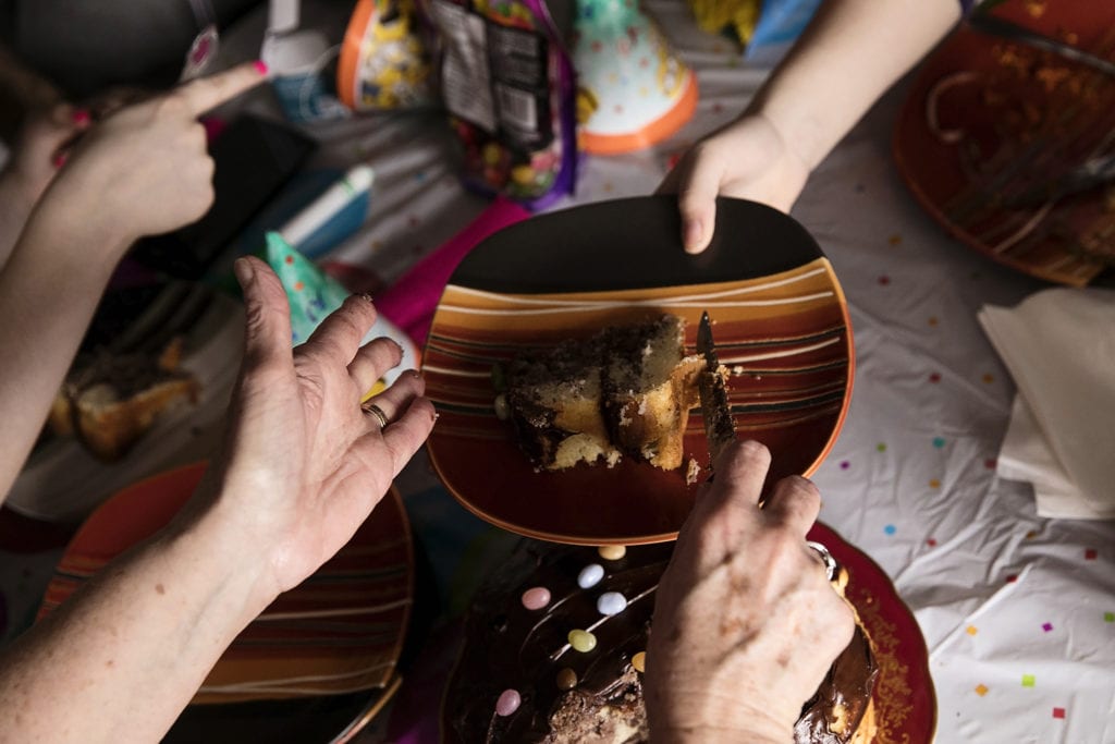hands slicing cake while child holds plate