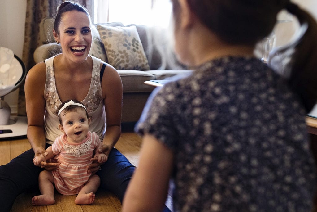 Mom sitting with baby on floor smiling at older daughter during Cornwall family photojournalism session