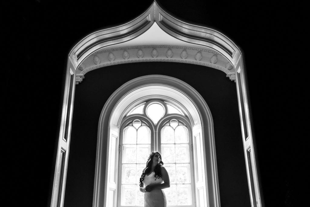 bride stands in front of window on wedding day at Strathmere Inn