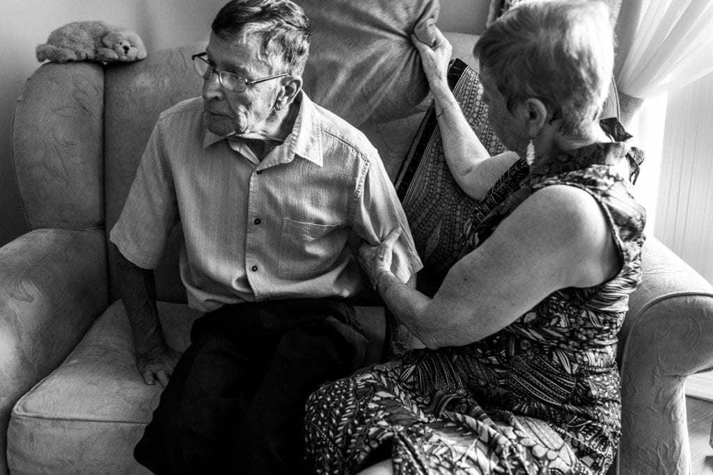 wife adjust pillows behind husband's back during documentary anniversary session