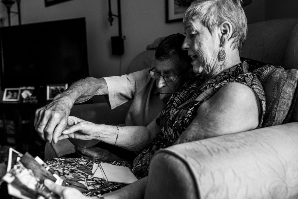 husband leans across wife and sticks out tongue while reaching for photos during documentary anniversary session