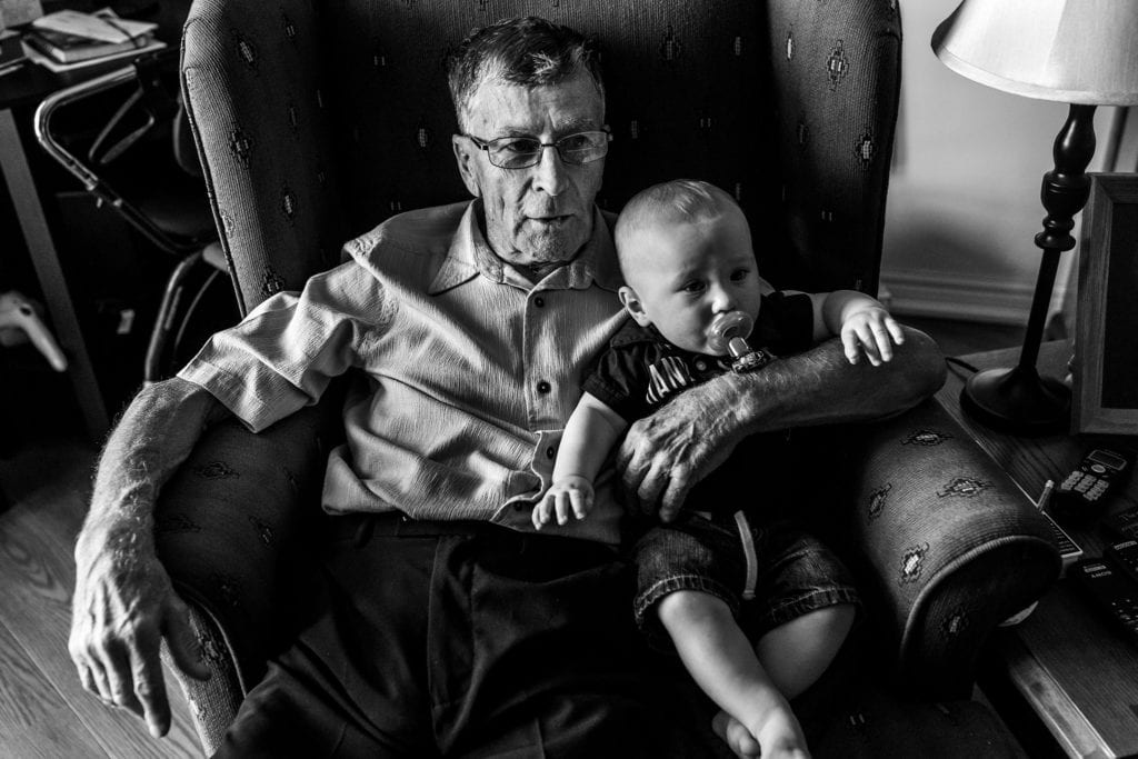 grandpa holds grandson while sitting in wingback chair