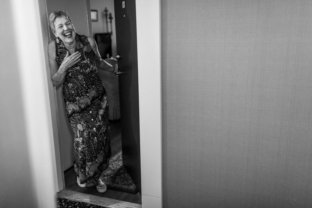 grandmother laughs in doorway with hand to chest
