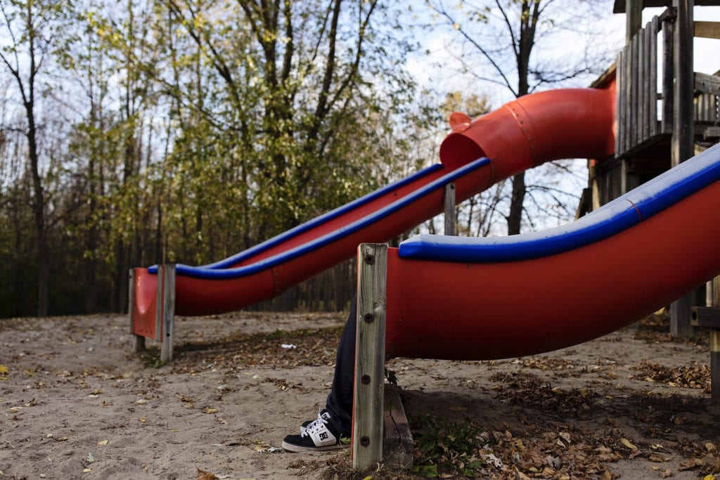 man lies down on slide in empty playground so that only feet are visible