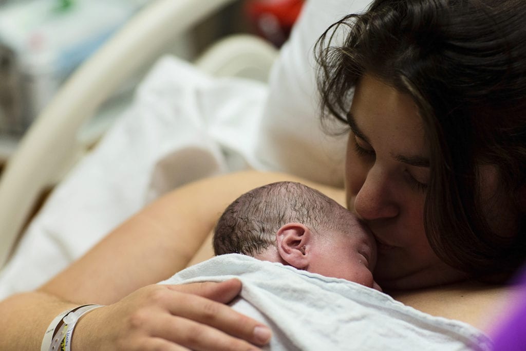 mom kisses new baby in hospital bed