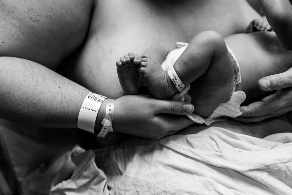 mom wearing hospital bracelet cradles newborn son's feet