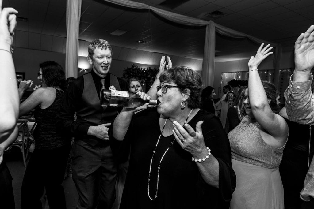 woman dancing while drinking from bottle of wine during wedding reception