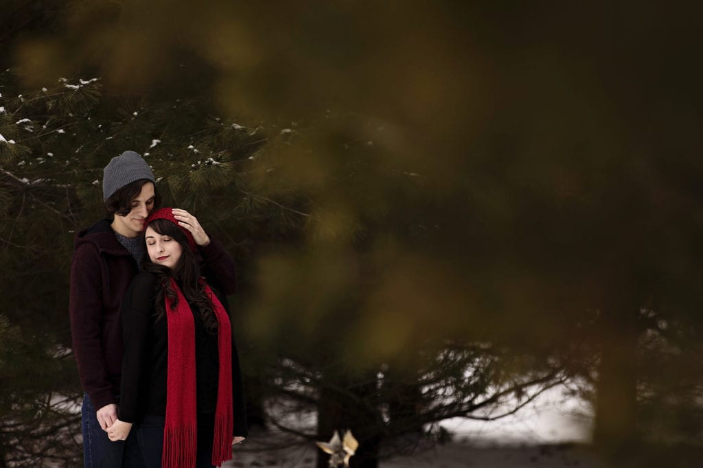 man in beanie and woman in red scarf share a quiet moment in winter engagement session
