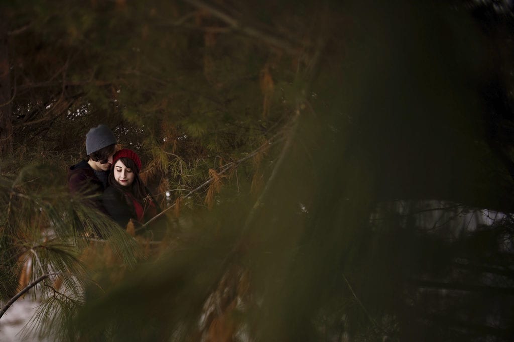 Young couple embracing in winter forest engagement shoot
