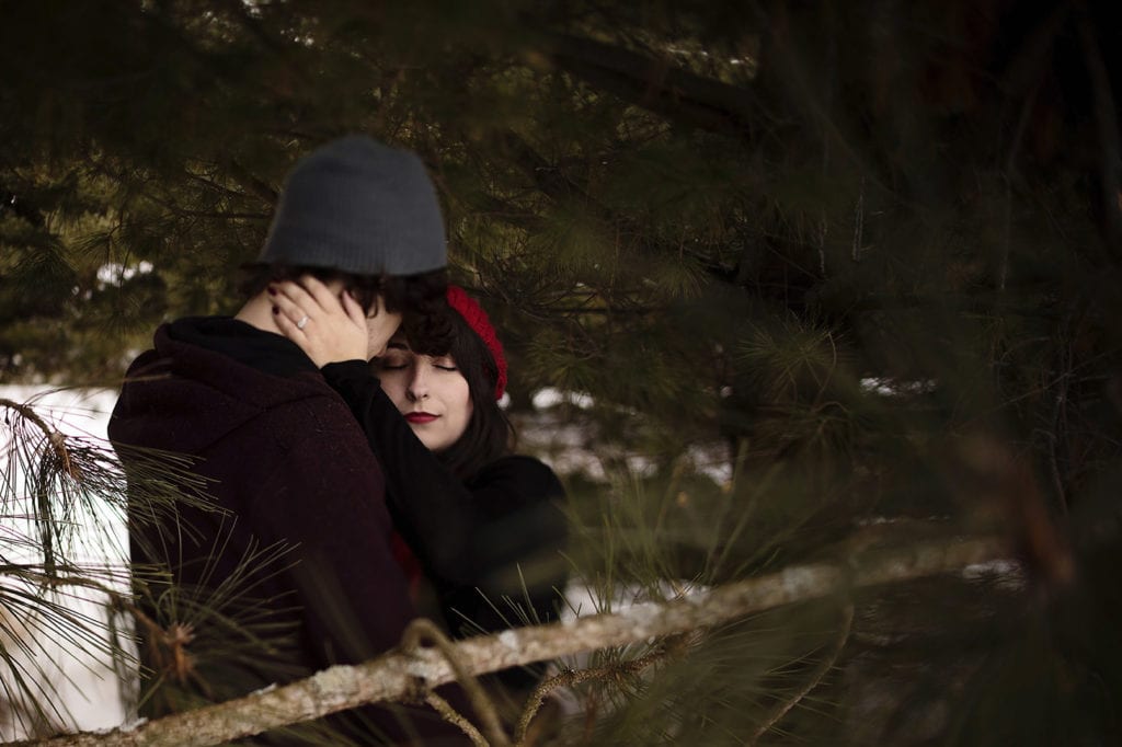 WInter couple nestled together in pine grove during engagement session