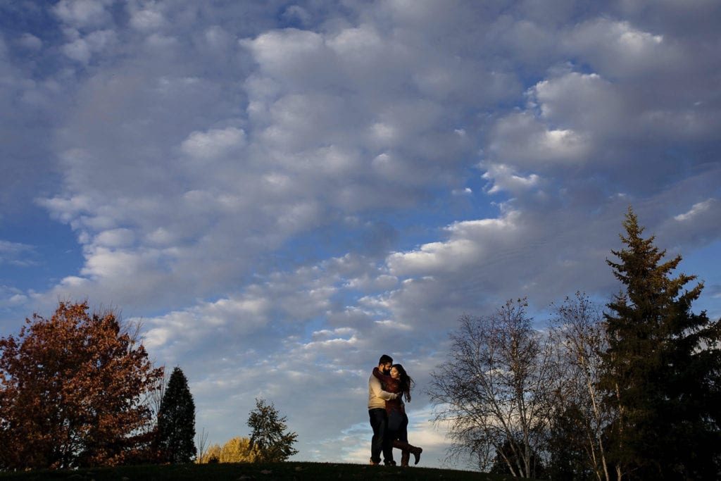 couple on hilltop against puffy clouds and blue sky in Cornwall Autumn Engagement Session