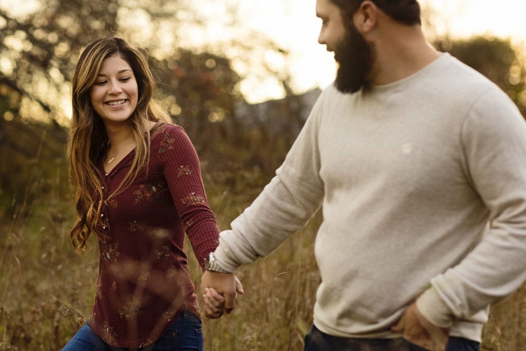 couple holding hands as they walk through field un Cornwall Autumn Engagement Session