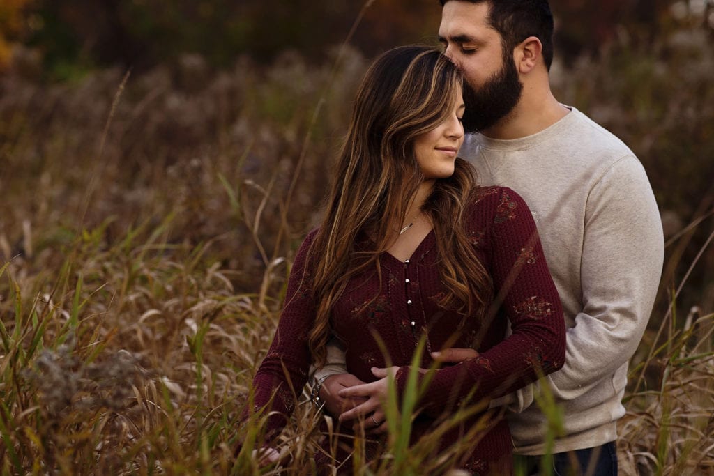 woman nestled against man in tall grass during romantic Cornwall Autumn Engagement Session
