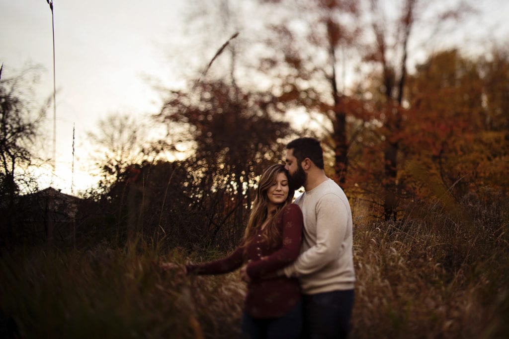man kissing woman's head in tall grasses during Cornwall Autumn Engagement Session