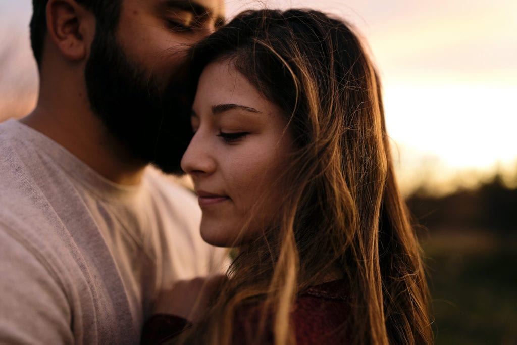 woman with windswept hair being held by man at sunset in Cornwall Autumn Engagement Session