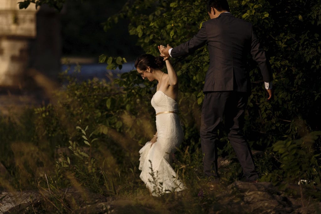 groom helping bride in mermaid lace gown step along shore in intimate ottawa park wedding