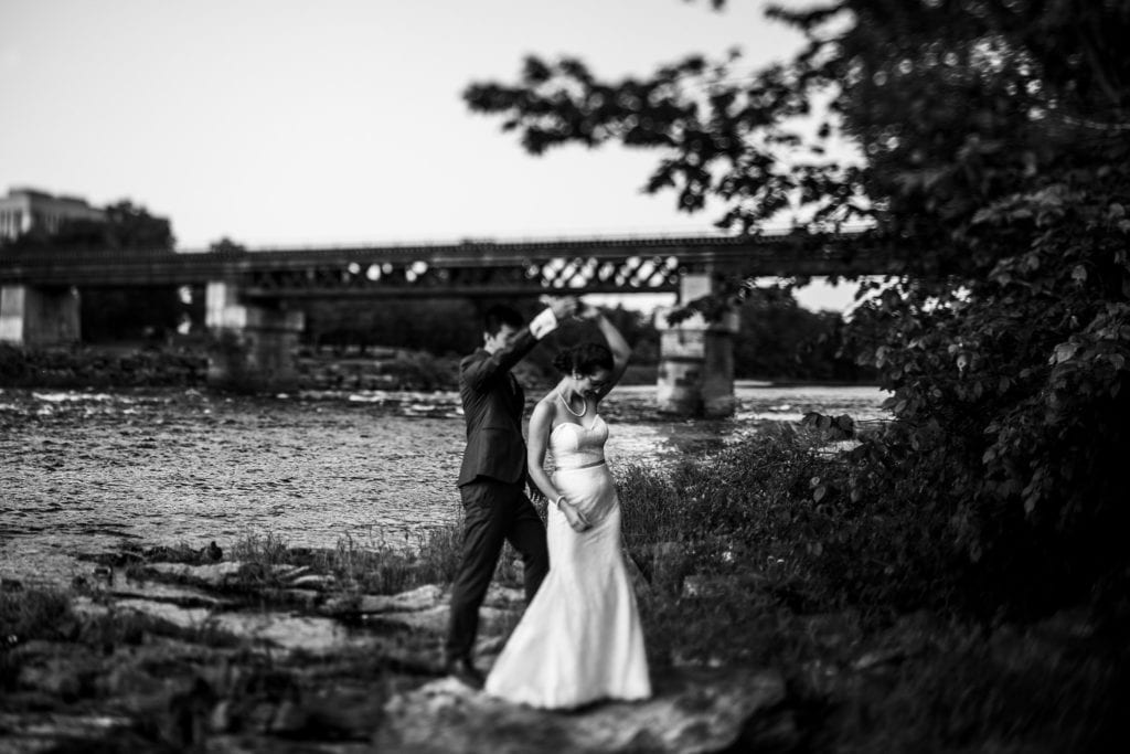 groom helping bride step along rocky shore in intimate Ottawa park wedding