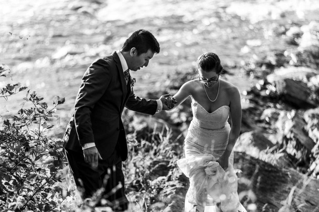 groom helps bride on rocky shore in intimate vincent massey park wedding