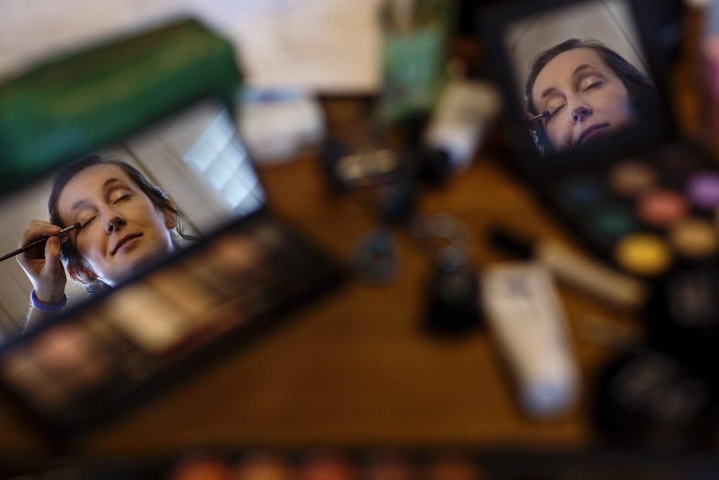 bride reflected in makeup mirrors as she gets eye shadow applied