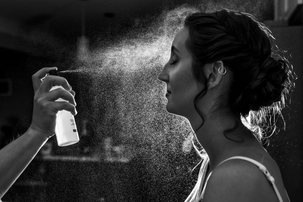 bride gets misted with finishing spray by makeup artist