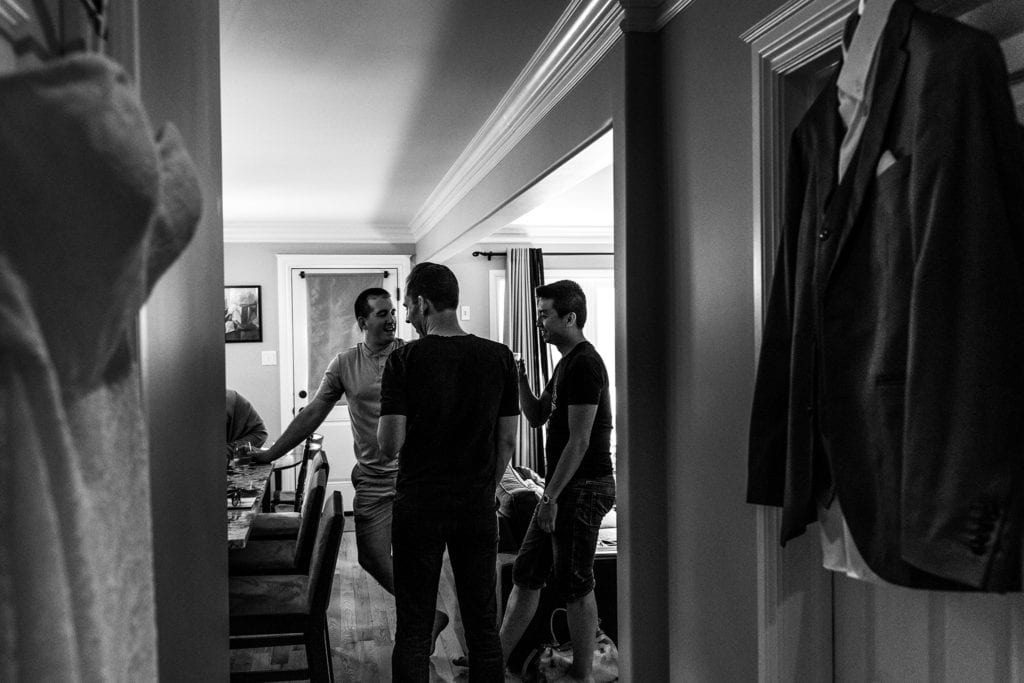 three men stand talking while wedding dress and suit hang in foreground