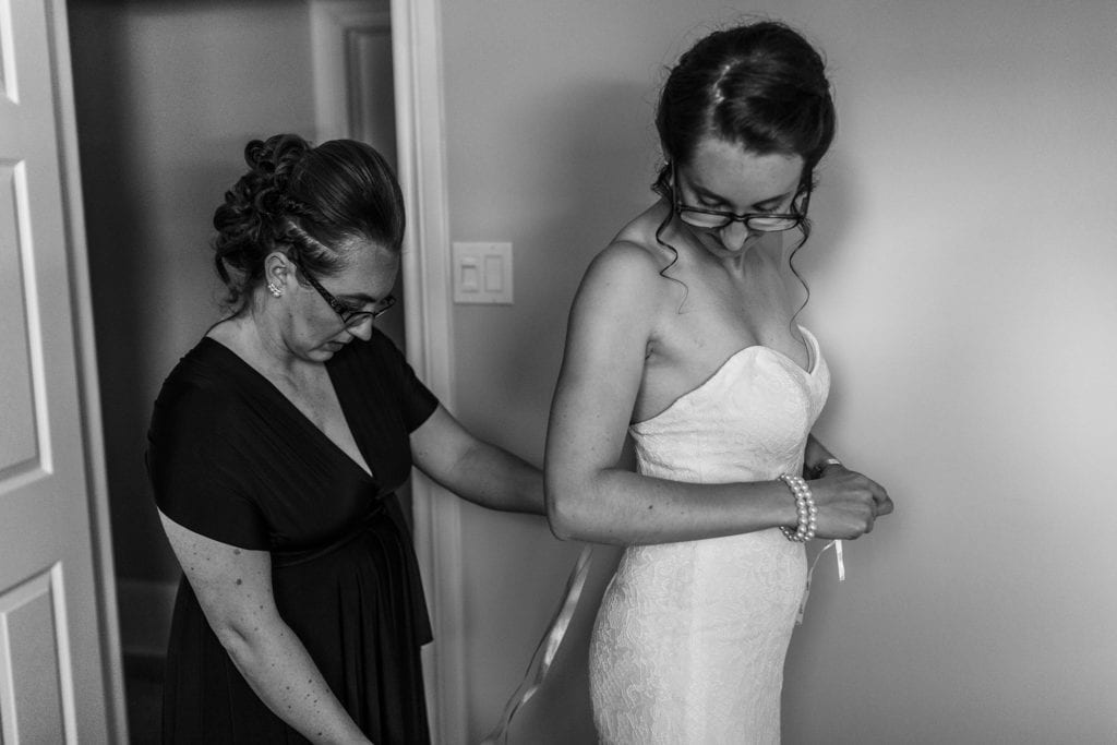 bride looks over shoulder as sister fastens ribbon around her dress